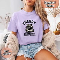 May include a black and white raccoon illustration with a tired, unbothered expression, holding a coffee cup, and bold text that reads “ENERGY UNMATCHED. UNMEDICATED. UNAPOLOGETIC.” conveying raw, unapologetic humor and mood.
