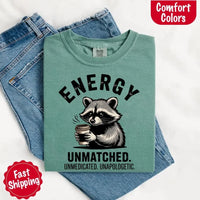 May include a black and white raccoon illustration with a tired, unbothered expression, holding a coffee cup, and bold text that reads “ENERGY UNMATCHED. UNMEDICATED. UNAPOLOGETIC.” conveying raw, unapologetic humor and mood.