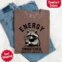 May include a black and white raccoon illustration with a tired, unbothered expression, holding a coffee cup, and bold text that reads “ENERGY UNMATCHED. UNMEDICATED. UNAPOLOGETIC.” conveying raw, unapologetic humor and mood.