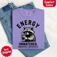 May include a black and white raccoon illustration with a tired, unbothered expression, holding a coffee cup, and bold text that reads “ENERGY UNMATCHED. UNMEDICATED. UNAPOLOGETIC.” conveying raw, unapologetic humor and mood.