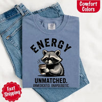 May include a black and white raccoon illustration with a tired, unbothered expression, holding a coffee cup, and bold text that reads “ENERGY UNMATCHED. UNMEDICATED. UNAPOLOGETIC.” conveying raw, unapologetic humor and mood.