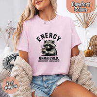 May include a black and white raccoon illustration with a tired, unbothered expression, holding a coffee cup, and bold text that reads “ENERGY UNMATCHED. UNMEDICATED. UNAPOLOGETIC.” conveying raw, unapologetic humor and mood.