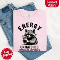 May include a black and white raccoon illustration with a tired, unbothered expression, holding a coffee cup, and bold text that reads “ENERGY UNMATCHED. UNMEDICATED. UNAPOLOGETIC.” conveying raw, unapologetic humor and mood.