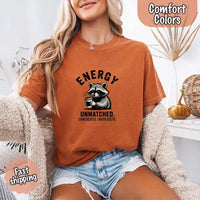 May include a black and white raccoon illustration with a tired, unbothered expression, holding a coffee cup, and bold text that reads “ENERGY UNMATCHED. UNMEDICATED. UNAPOLOGETIC.” conveying raw, unapologetic humor and mood.