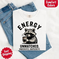 May include a black and white raccoon illustration with a tired, unbothered expression, holding a coffee cup, and bold text that reads “ENERGY UNMATCHED. UNMEDICATED. UNAPOLOGETIC.” conveying raw, unapologetic humor and mood.