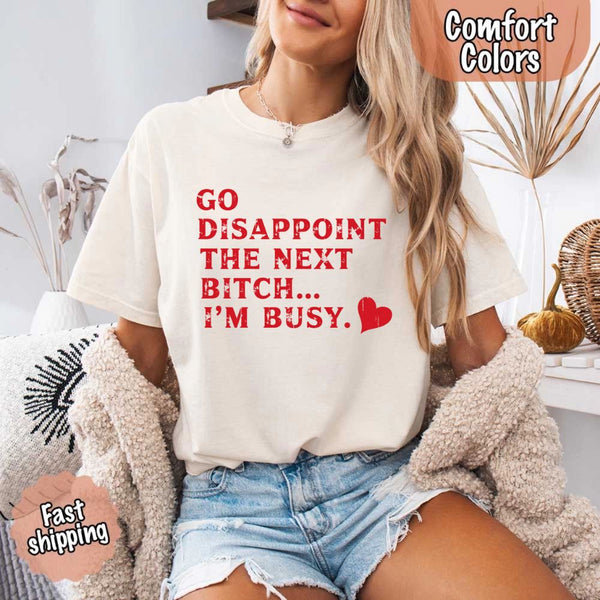 May include bold red distressed typography with the phrase “Go Disappoint The Next Bitch… I’m Busy.” alongside a red heart, expressing sass, confidence, and attitude.