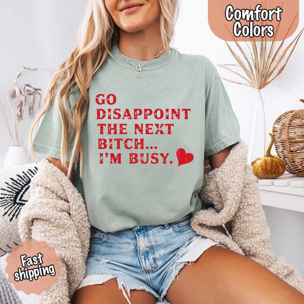 May include bold red distressed typography with the phrase “Go Disappoint The Next Bitch… I’m Busy.” alongside a red heart, expressing sass, confidence, and attitude.