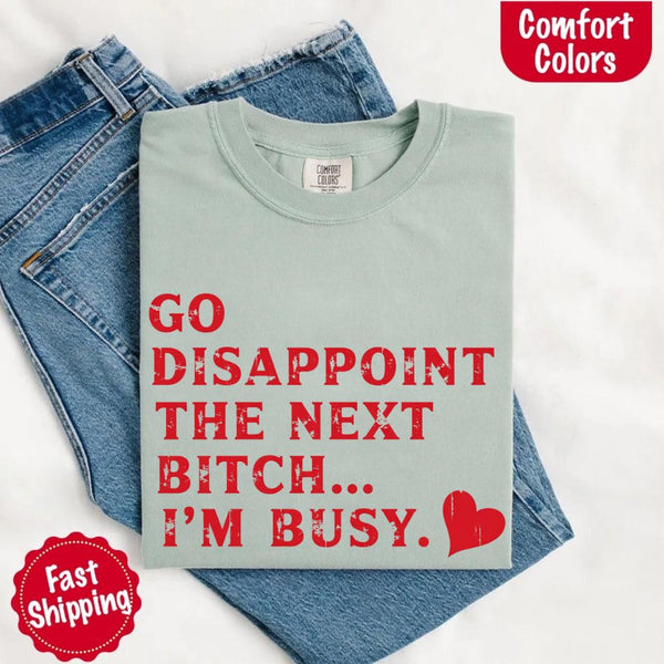 May include bold red distressed typography with the phrase “Go Disappoint The Next Bitch… I’m Busy.” alongside a red heart, expressing sass, confidence, and attitude.