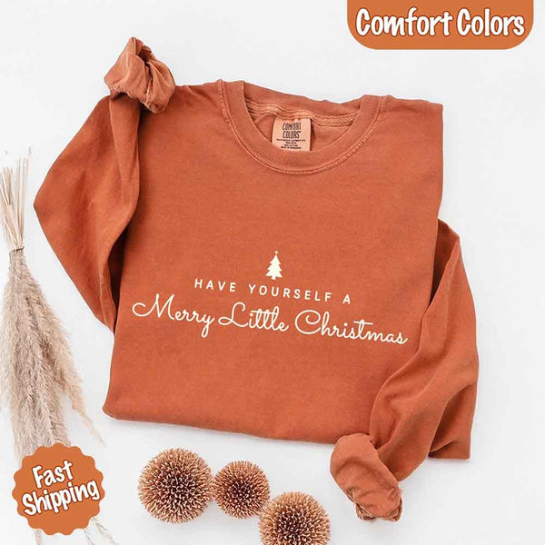May include a Comfort Colors long sleeve shirt featuring the phrase “Have Yourself a Merry Christmas” in festive print, displayed flat with soft cotton texture and seasonal tones.