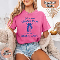 May Include: Comfort Colors t-shirt with a vintage-style blue graphic that features a cheerful raccoon popping out of a trash can with its arms raised. The design includes playful, curved typography that reads 'Let’s be more TRASH CAN' above the raccoon and 'and less TRASH CAN’T' below it. The raccoon has a big smile and cartoon eyes, giving the shirt a humorous and uplifting feel. Ideal for motivational, funny, or animal-themed apparel collections