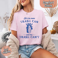 May Include: Comfort Colors t-shirt with a vintage-style blue graphic that features a cheerful raccoon popping out of a trash can with its arms raised. The design includes playful, curved typography that reads 'Let’s be more TRASH CAN' above the raccoon and 'and less TRASH CAN’T' below it. The raccoon has a big smile and cartoon eyes, giving the shirt a humorous and uplifting feel. Ideal for motivational, funny, or animal-themed apparel collections