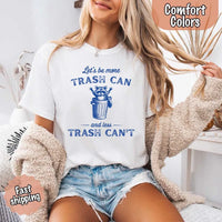 May Include: Comfort Colors t-shirt with a vintage-style blue graphic that features a cheerful raccoon popping out of a trash can with its arms raised. The design includes playful, curved typography that reads 'Let’s be more TRASH CAN' above the raccoon and 'and less TRASH CAN’T' below it. The raccoon has a big smile and cartoon eyes, giving the shirt a humorous and uplifting feel. Ideal for motivational, funny, or animal-themed apparel collections