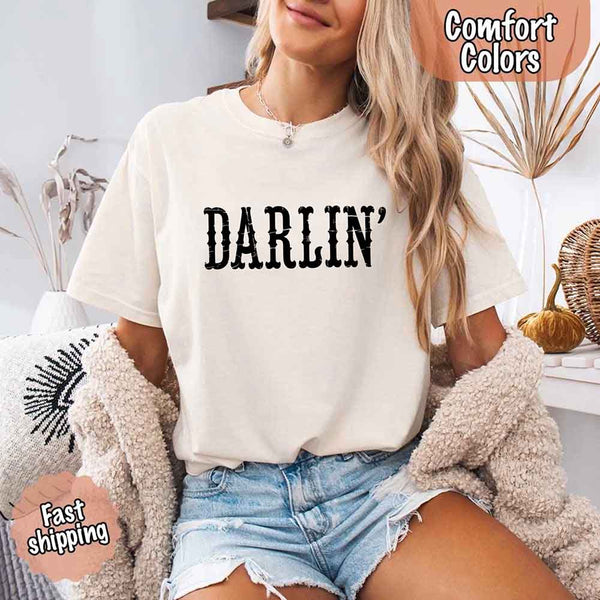 May include bold black distressed Western-style typography featuring the word “Darlin’,” evoking country charm with a vintage, rustic feel.