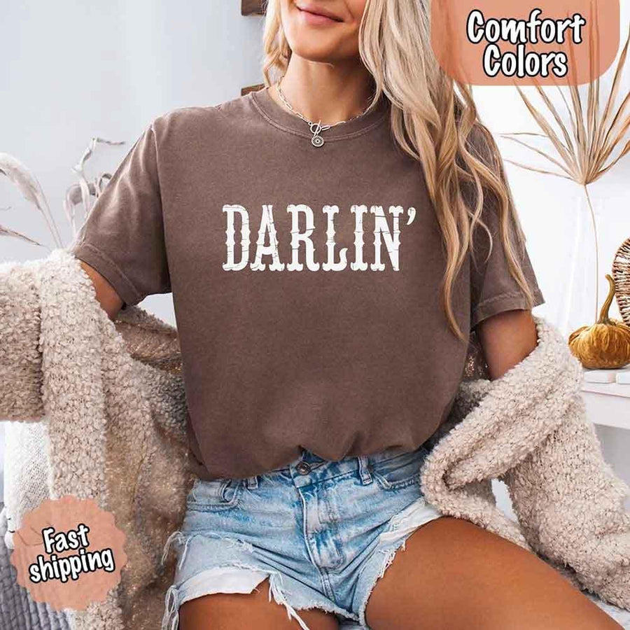 May include bold black distressed Western-style typography featuring the word “Darlin’,” evoking country charm with a vintage, rustic feel.