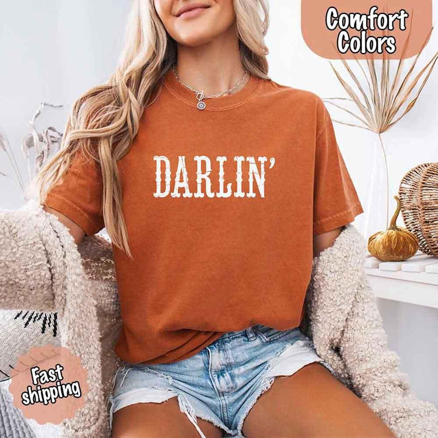 May include bold black distressed Western-style typography featuring the word “Darlin’,” evoking country charm with a vintage, rustic feel.
