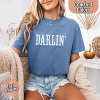 May include bold black distressed Western-style typography featuring the word “Darlin’,” evoking country charm with a vintage, rustic feel.