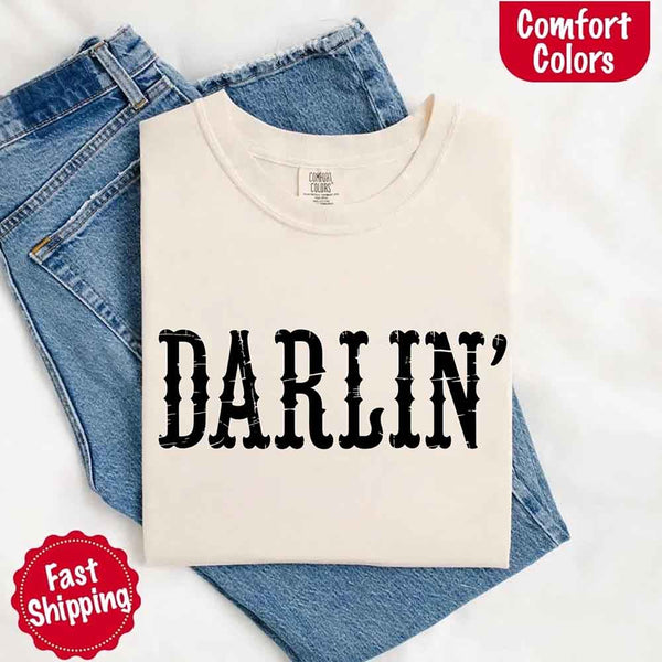 May include bold black distressed Western-style typography featuring the word “Darlin’,” evoking country charm with a vintage, rustic feel.