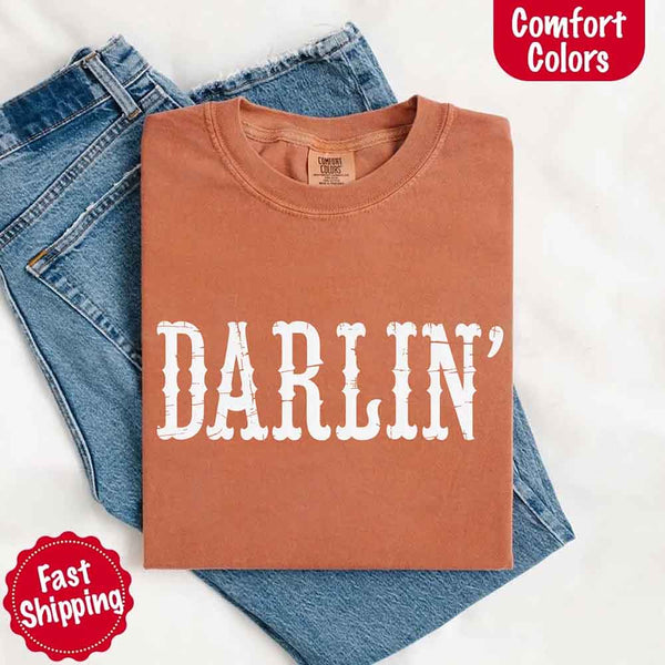 May include bold black distressed Western-style typography featuring the word “Darlin’,” evoking country charm with a vintage, rustic feel.