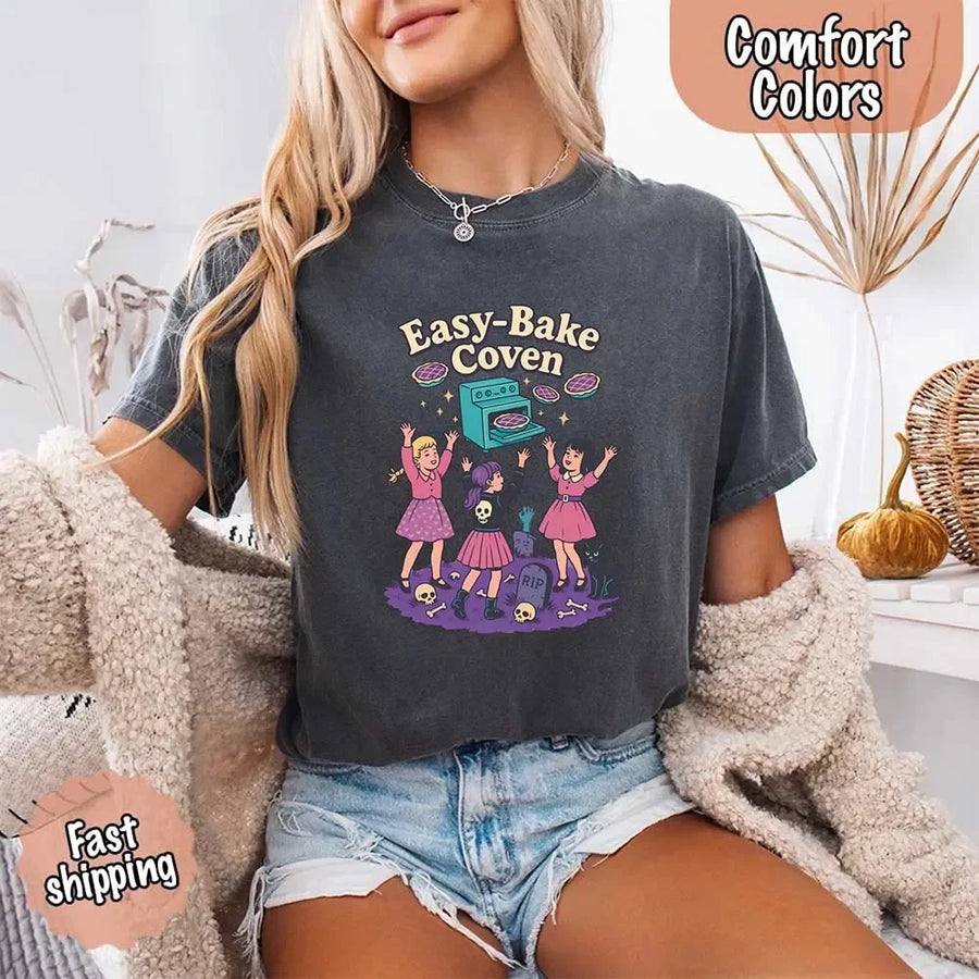 May include Easy Bake Coven graphic with three witch girls baking pies, retro oven, skulls, gravestone, and black cat – vintage 90s Halloween shirt.