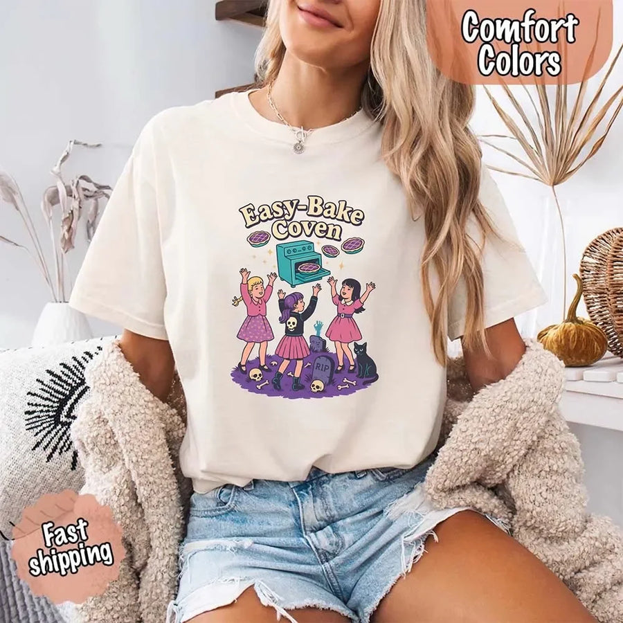 May include Easy Bake Coven graphic with three witch girls baking pies, retro oven, skulls, gravestone, and black cat – vintage 90s Halloween shirt.