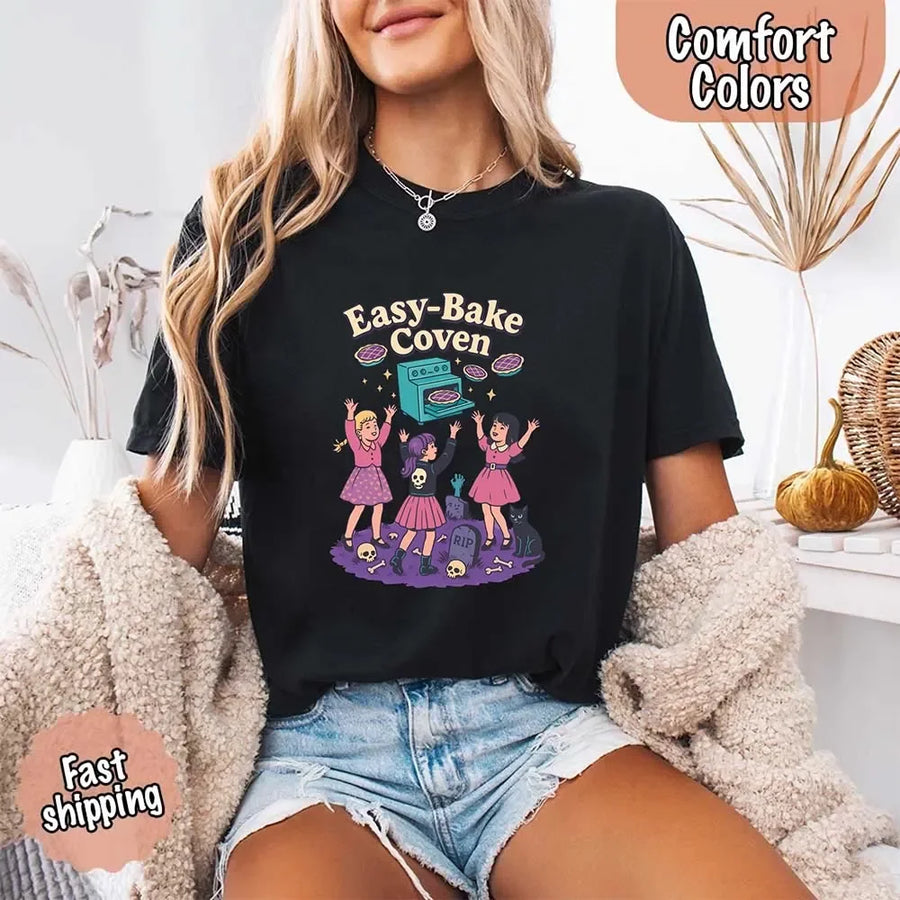 May include Easy Bake Coven graphic with three witch girls baking pies, retro oven, skulls, gravestone, and black cat – vintage 90s Halloween shirt.