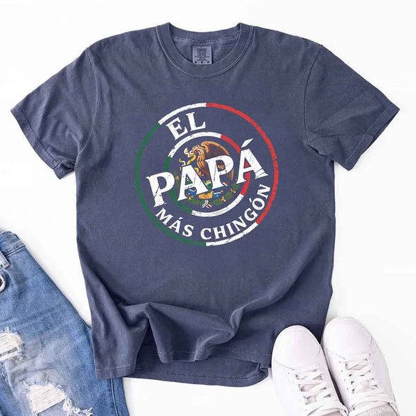 May include bold distressed text that reads “El Papá Más Chingón” over a circular Mexican flag-inspired design with an eagle emblem, celebrating proud and confident fatherhood with cultural pride.