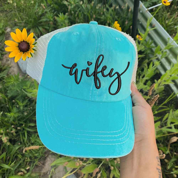 May include an embroidered pigment-dyed trucker hat with mesh back, featuring “Wifey” or “Hubby” text, designed as a casual and stylish gift for spouses or anniversaries.