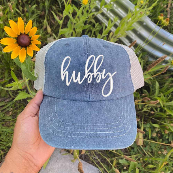 May include an embroidered pigment-dyed trucker hat with mesh back, featuring “Wifey” or “Hubby” text, designed as a casual and stylish gift for spouses or anniversaries.