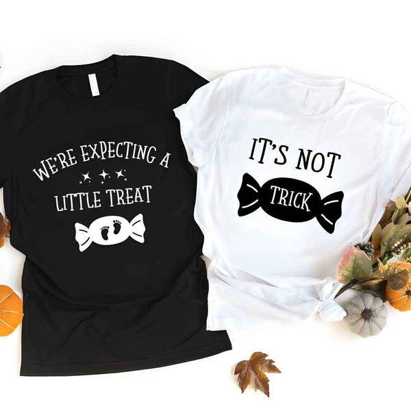 May include matching couple Halloween pregnancy announcement shirts, one reading ‘We’re Expecting a Little Treat’ with candy and baby footprints, and the other reading ‘It’s Not Trick’ with candy graphic – fun maternity reveal apparel.