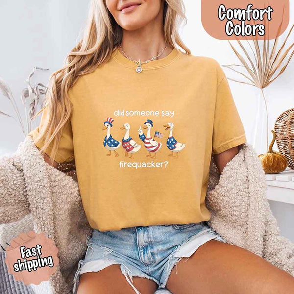 Person wearing a mustard yellow t-shirt with a graphic of ducks and text, sitting on a couch.