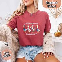 Person wearing a red t-shirt with a graphic of ducks and text, sitting indoors.
