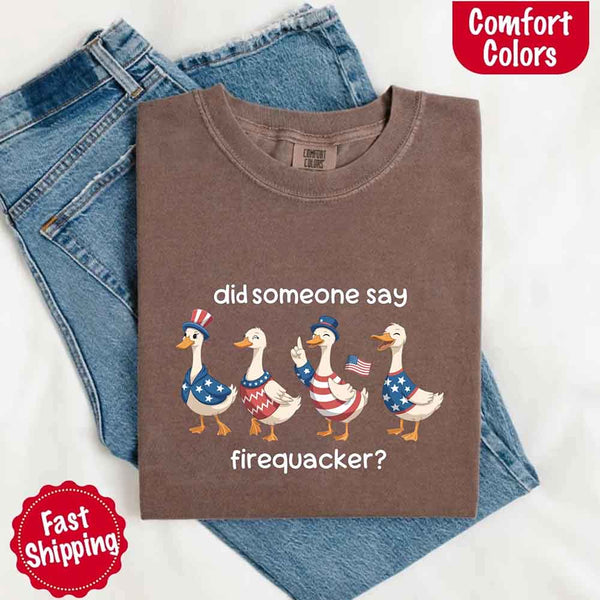 Folded brown t-shirt with graphic design of ducks in American flags and text, placed on blue jeans with 'Comfort Colors' branding.