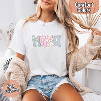 Woman wearing a white t-shirt with 'MAMA' printed in colorful letters, sitting on a couch.