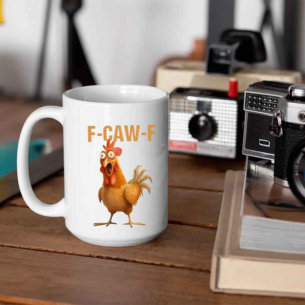 White mug with a cartoon chicken and 'F-CAW-F' text on a wooden surface with a vintage radio and camera in the background.