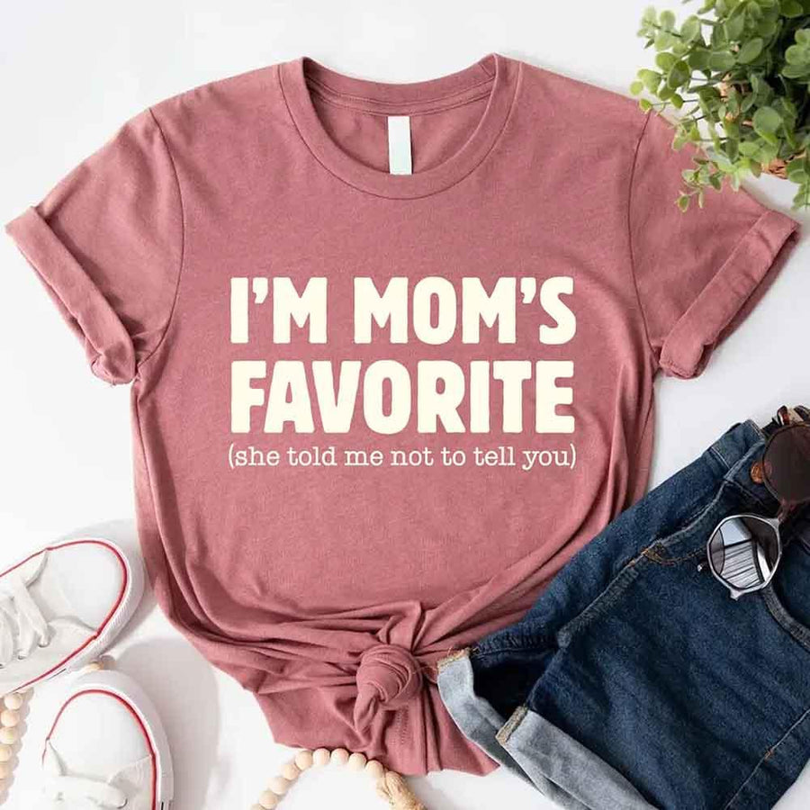 May include a unisex t-shirt reading “I’m Mom’s Favorite” in bold font, displayed on a flat lay or model, ideal for Mother’s Day gifting.