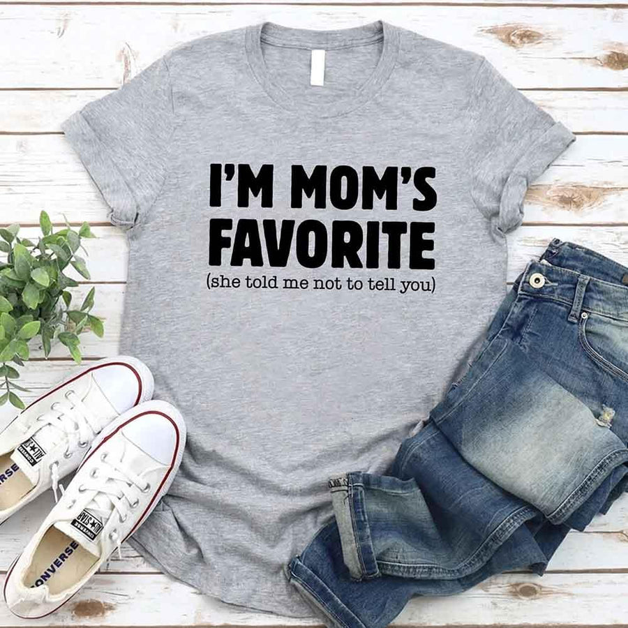 May include a unisex t-shirt reading “I’m Mom’s Favorite” in bold font, displayed on a flat lay or model, ideal for Mother’s Day gifting.