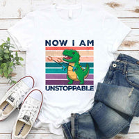White t-shirt with dinosaur graphic and text, paired with jeans and sneakers on a wooden surface.
