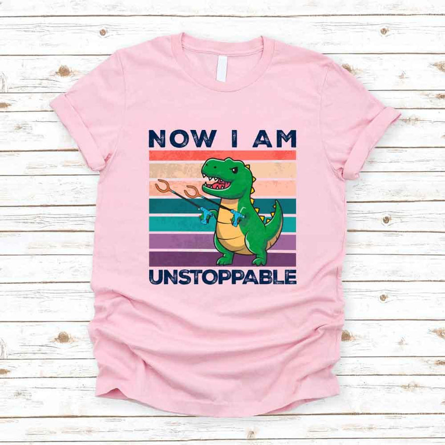 Pink t-shirt with a dinosaur graphic and text on a wooden surface
