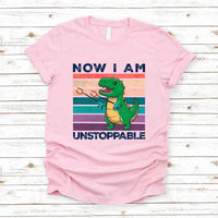 Pink t-shirt with a dinosaur graphic and text on a wooden surface