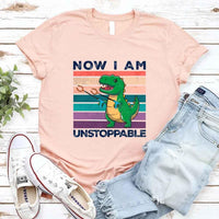 peach t-shirt with dinosaur graphic and text, paired with jeans and sneakers on a wooden surface.