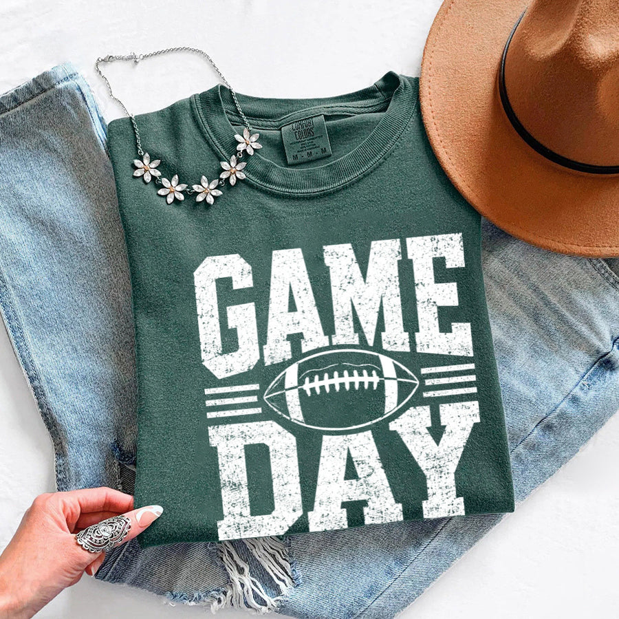 May include a Comfort Colors T-shirt featuring a distressed Game Day graphic with a football design, perfect for football fans, tailgates, watch parties, and sporting events.