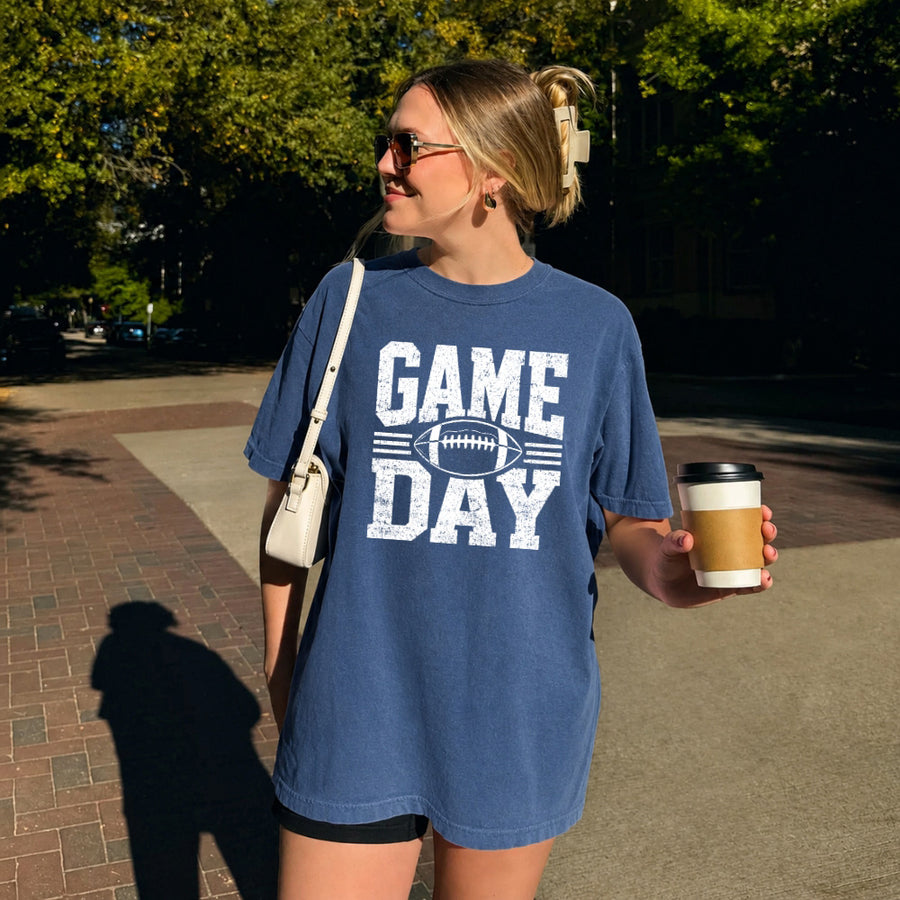 May include a Comfort Colors T-shirt featuring a distressed Game Day graphic with a football design, perfect for football fans, tailgates, watch parties, and sporting events.