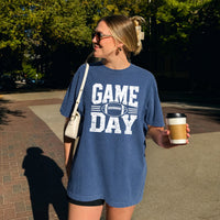 May include a Comfort Colors T-shirt featuring a distressed Game Day graphic with a football design, perfect for football fans, tailgates, watch parties, and sporting events.