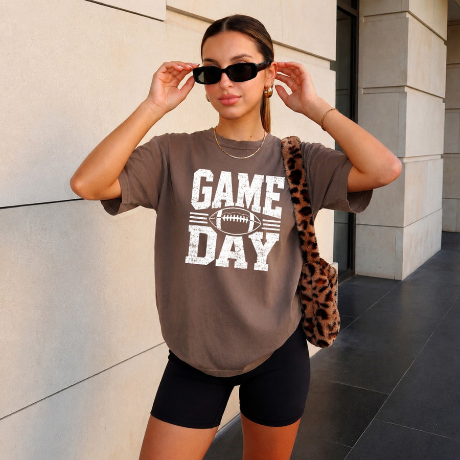 May include a Comfort Colors T-shirt featuring a distressed Game Day graphic with a football design, perfect for football fans, tailgates, watch parties, and sporting events.