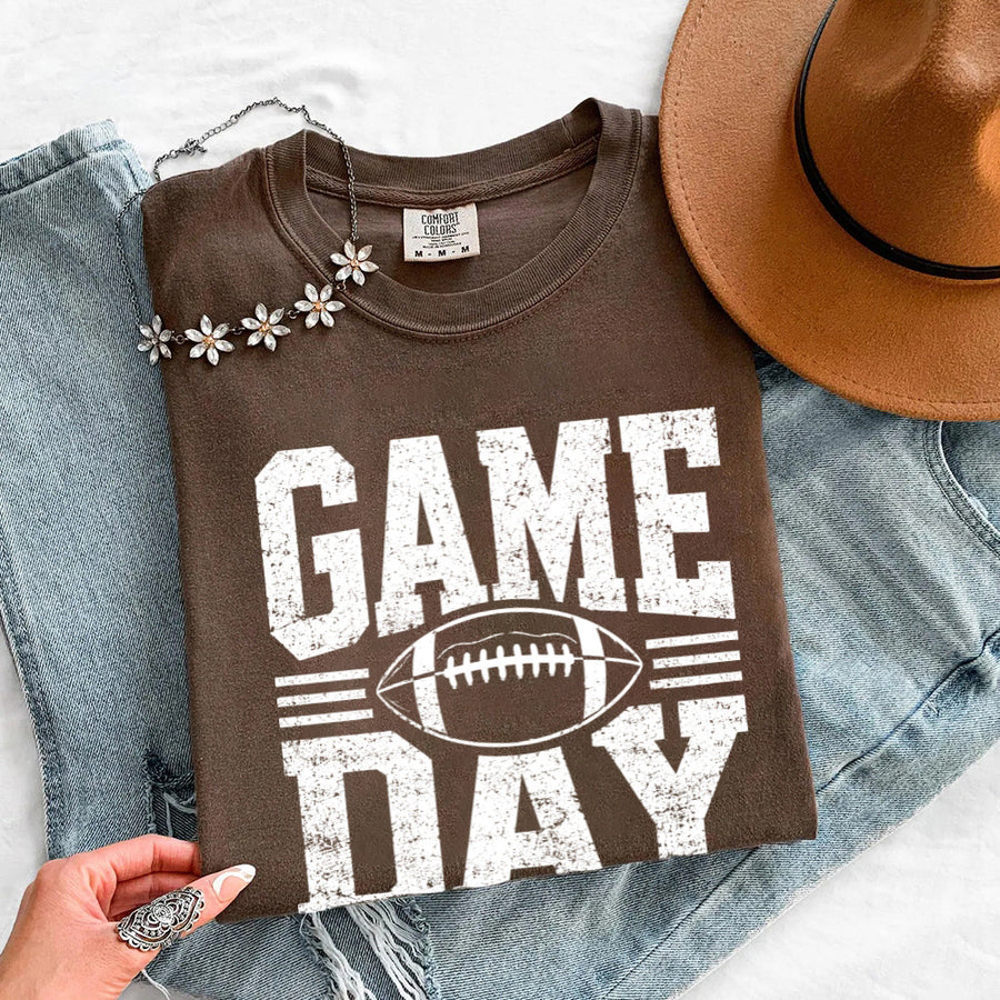 May include a Comfort Colors T-shirt featuring a distressed Game Day graphic with a football design, perfect for football fans, tailgates, watch parties, and sporting events.