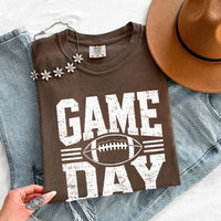 May include a Comfort Colors T-shirt featuring a distressed Game Day graphic with a football design, perfect for football fans, tailgates, watch parties, and sporting events.