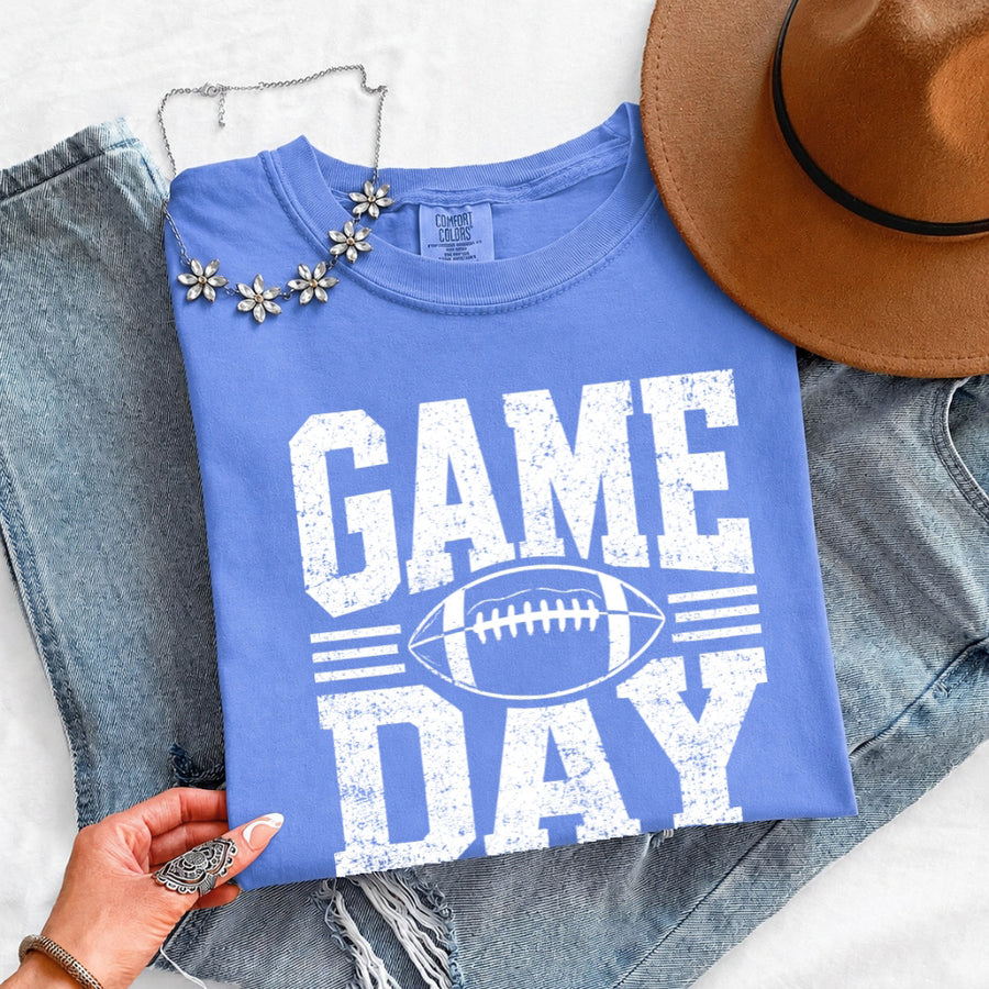May include a Comfort Colors T-shirt featuring a distressed Game Day graphic with a football design, perfect for football fans, tailgates, watch parties, and sporting events.