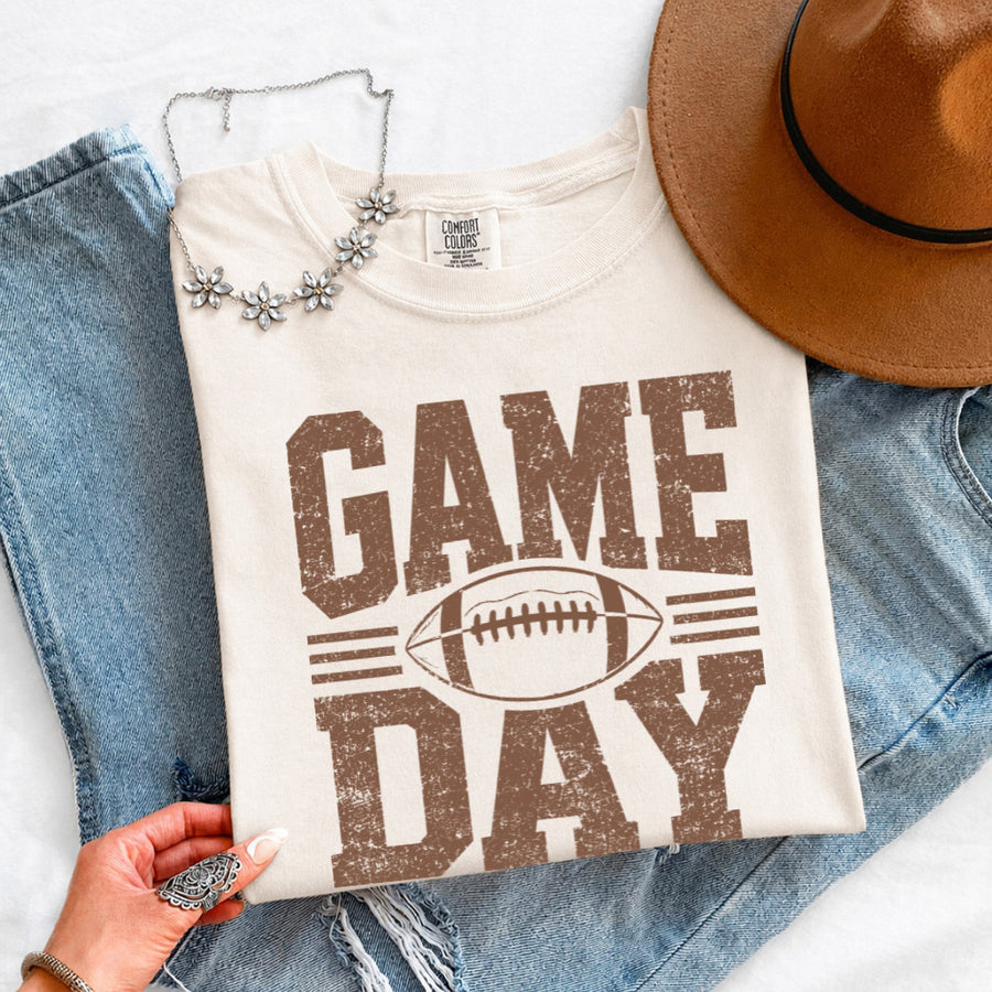 May include a Comfort Colors T-shirt featuring a distressed Game Day graphic with a football design, perfect for football fans, tailgates, watch parties, and sporting events.