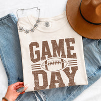 May include a Comfort Colors T-shirt featuring a distressed Game Day graphic with a football design, perfect for football fans, tailgates, watch parties, and sporting events.