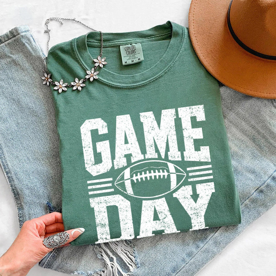 May include a Comfort Colors T-shirt featuring a distressed Game Day graphic with a football design, perfect for football fans, tailgates, watch parties, and sporting events.